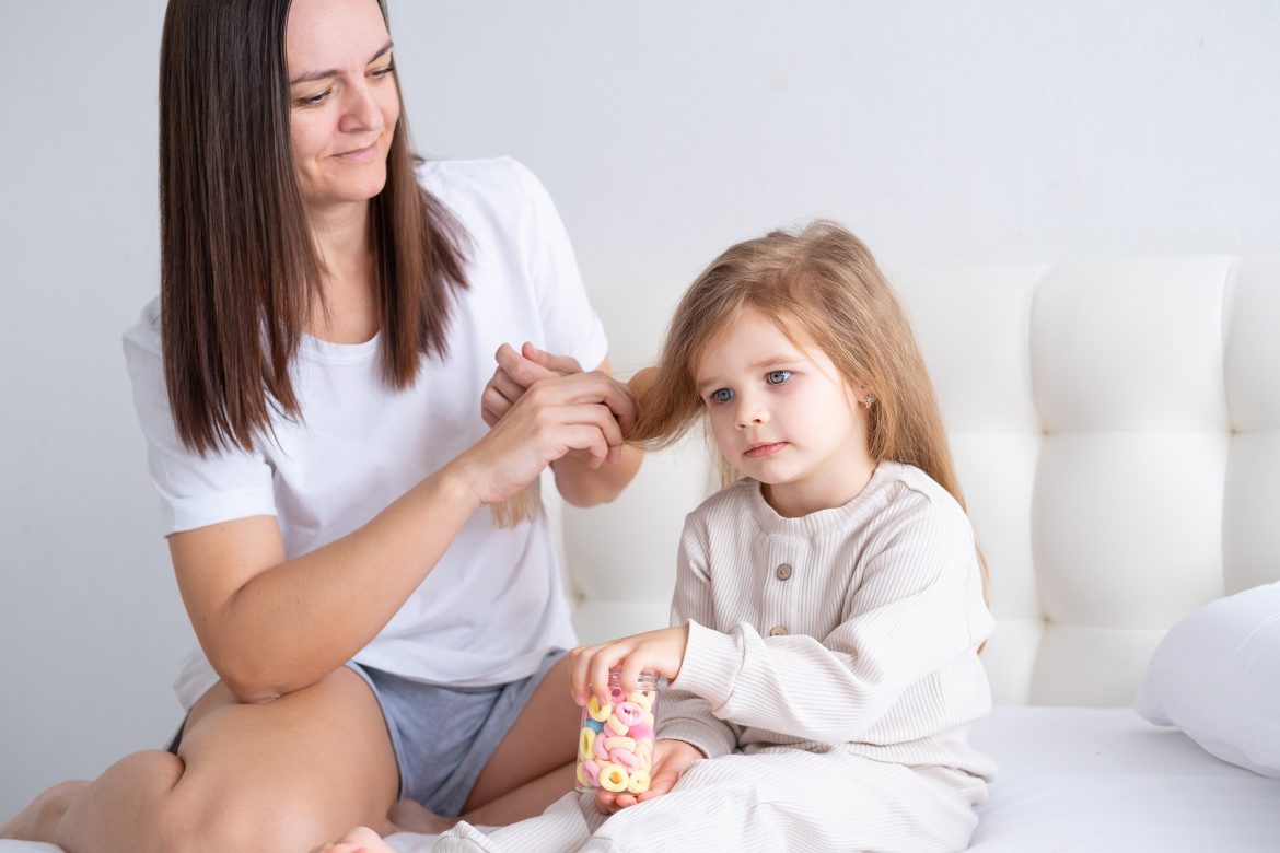 happy-mother-brushing-daughter-long-hair-with-eco-friendly-wooden-comb-sitting-bed-home